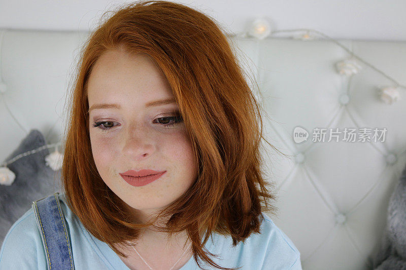 14 / 15岁的红发少女，苍白的皮肤和雀斑坐在卧室看着沉思和对自己微笑，沉思和反省的照片